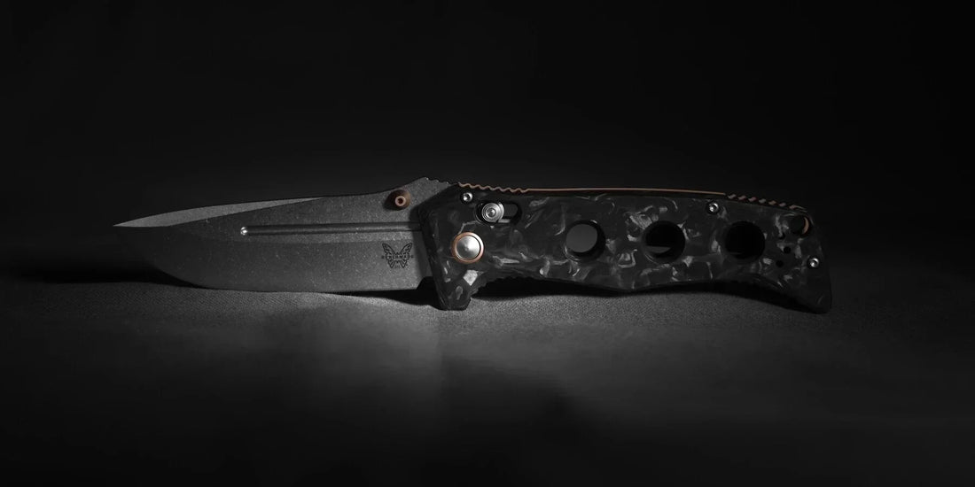 Benchmade Adamas in marbled carbon fiber with bronze hardware, open and photographed low-angle against a dark backdrop, emphasizing the blade edge and handle contours.